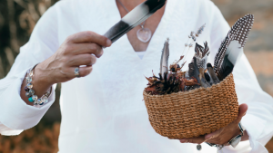 Woven basket of feathers and tools held by a person in a